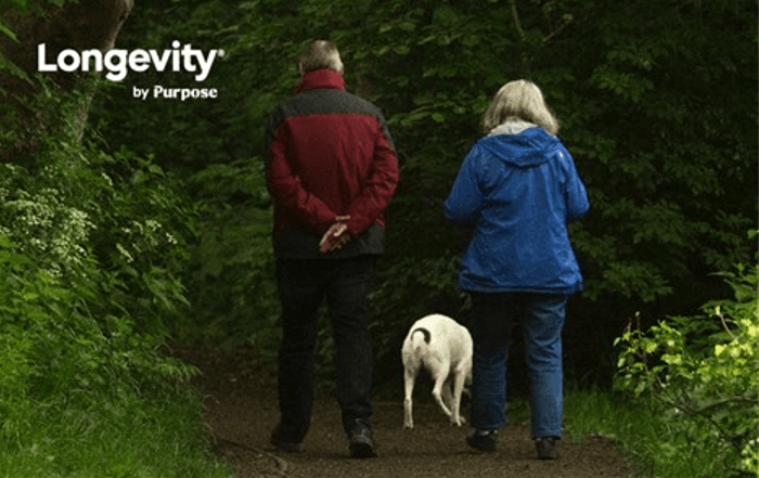 A picture of a man, a woman and a dog walking into the woods.